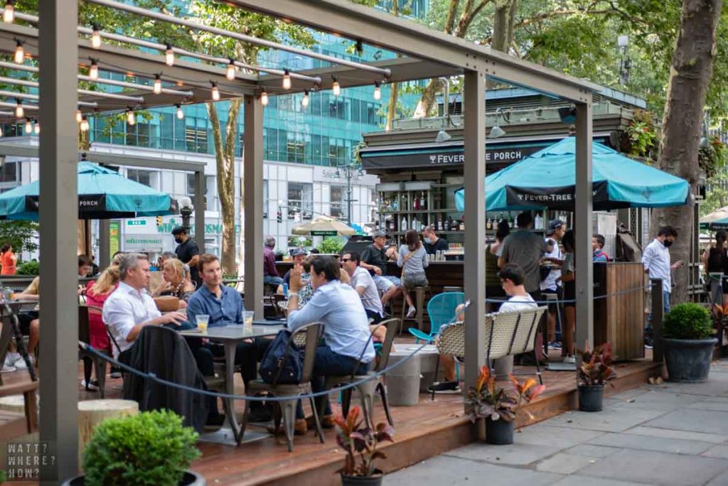 Fever-Tree Porch at Bryant Park NY is an open wooden deck with tables and swing loveseats. 